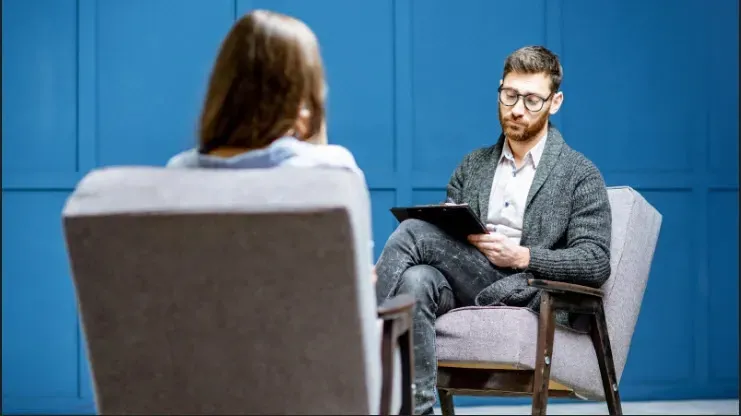 A man is sitting in a chair talking to a woman.