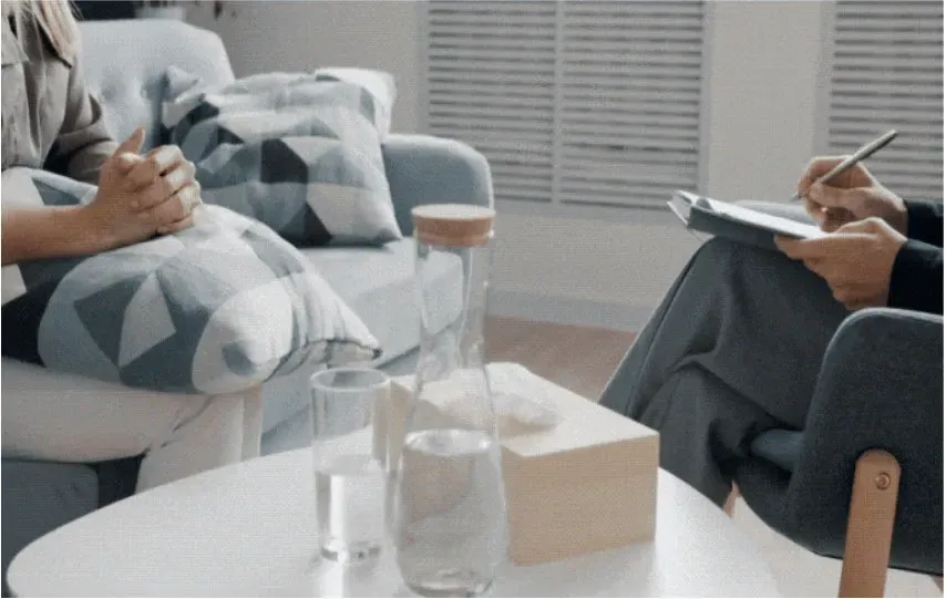 A man and a woman are sitting on a couch talking to each other.