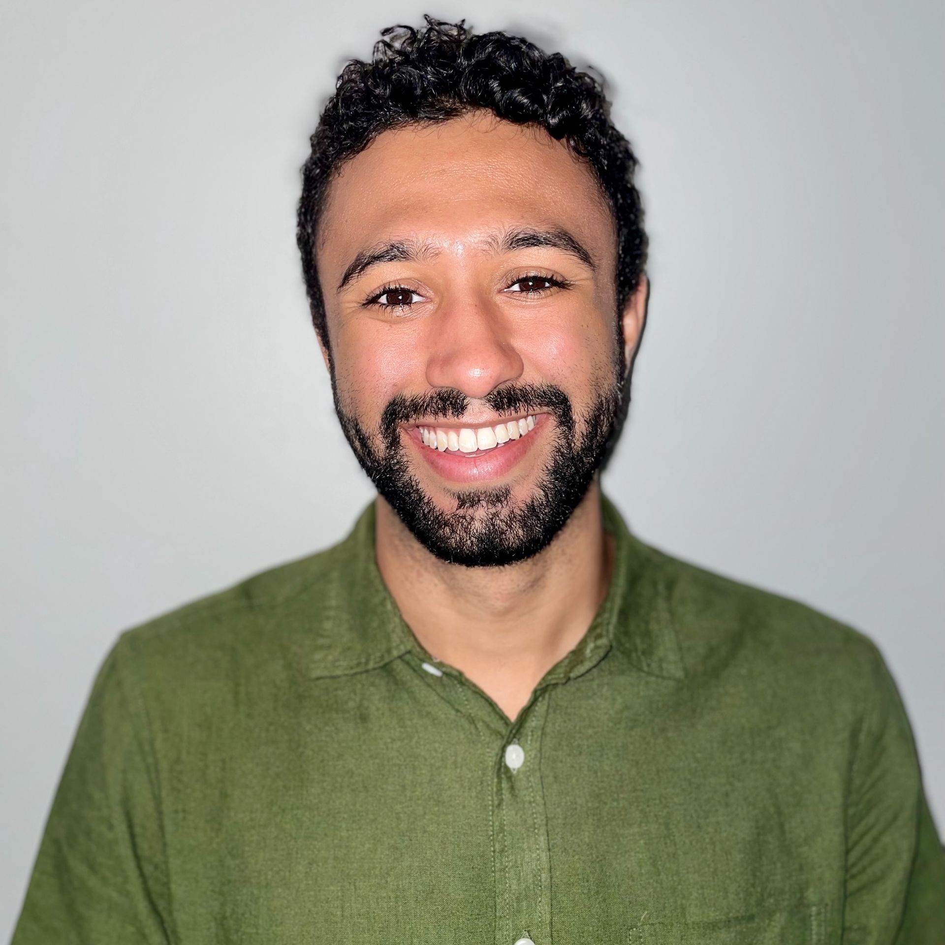 A man with a beard is wearing a green shirt and smiling.