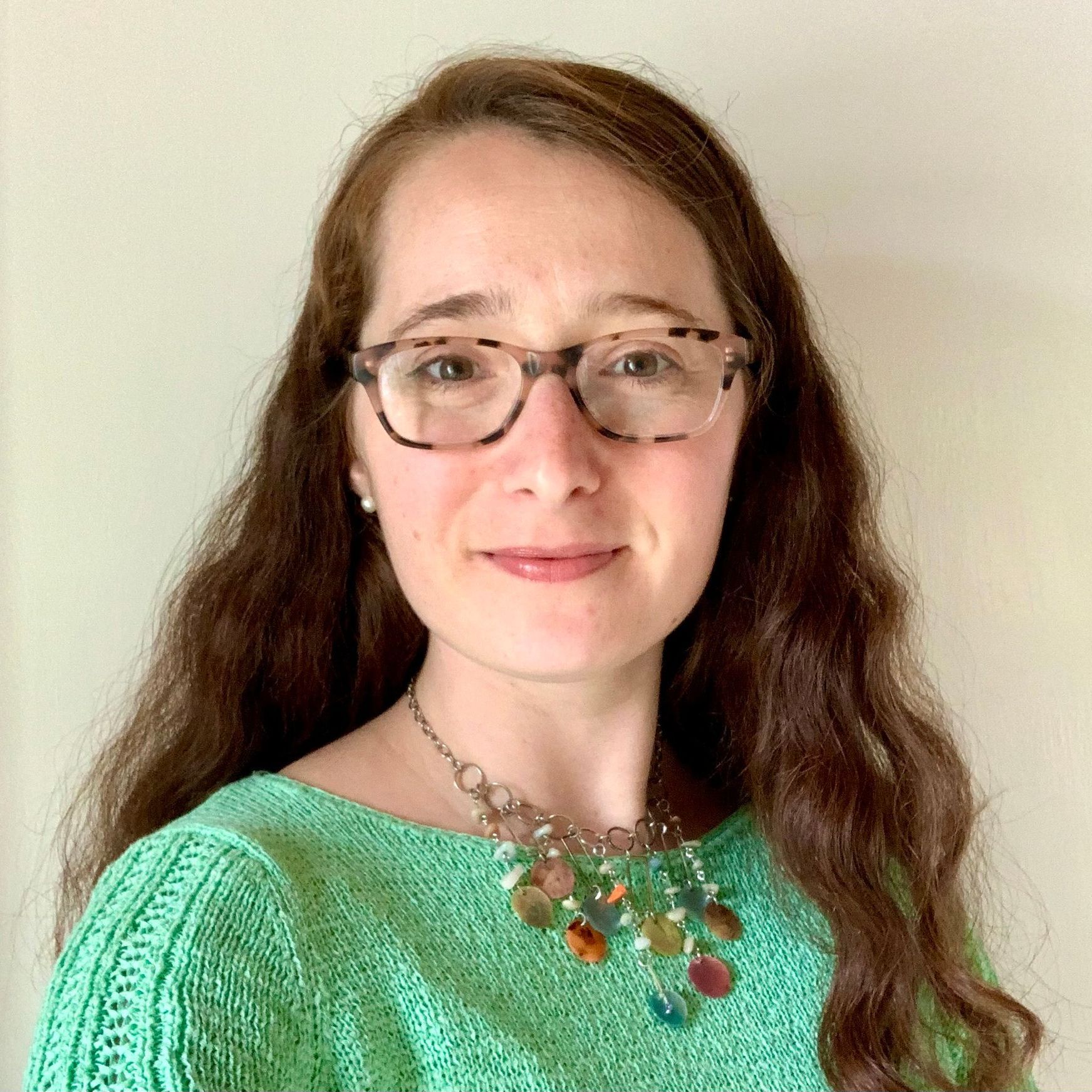 A woman wearing glasses and a green sweater is smiling for the camera.
