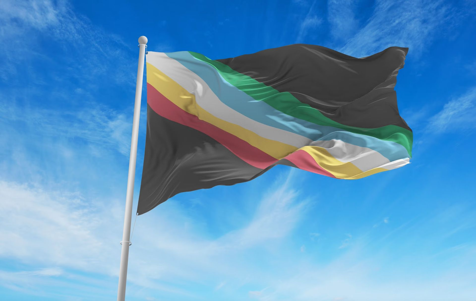 The disability pride flag flies in front of a blue sky.