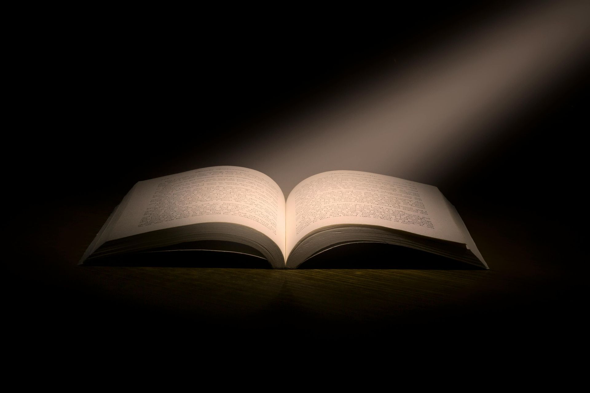 Open book illuminated by a beam of light against a dark background.