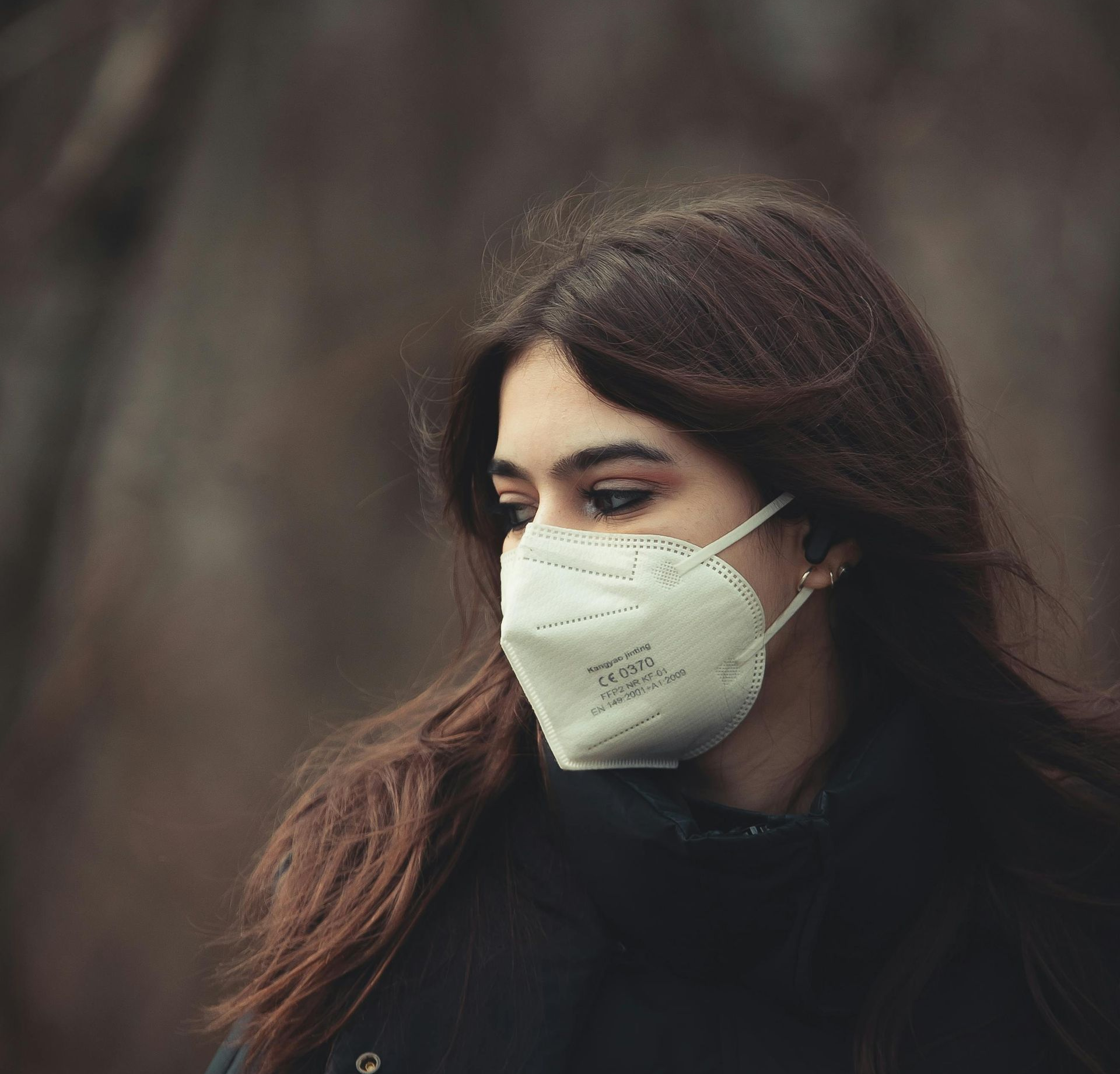 A person wearing a white KN95 respirator gazes into the distance pensively. A person wearing a white KN95 respirator gazes into the distance pensively.