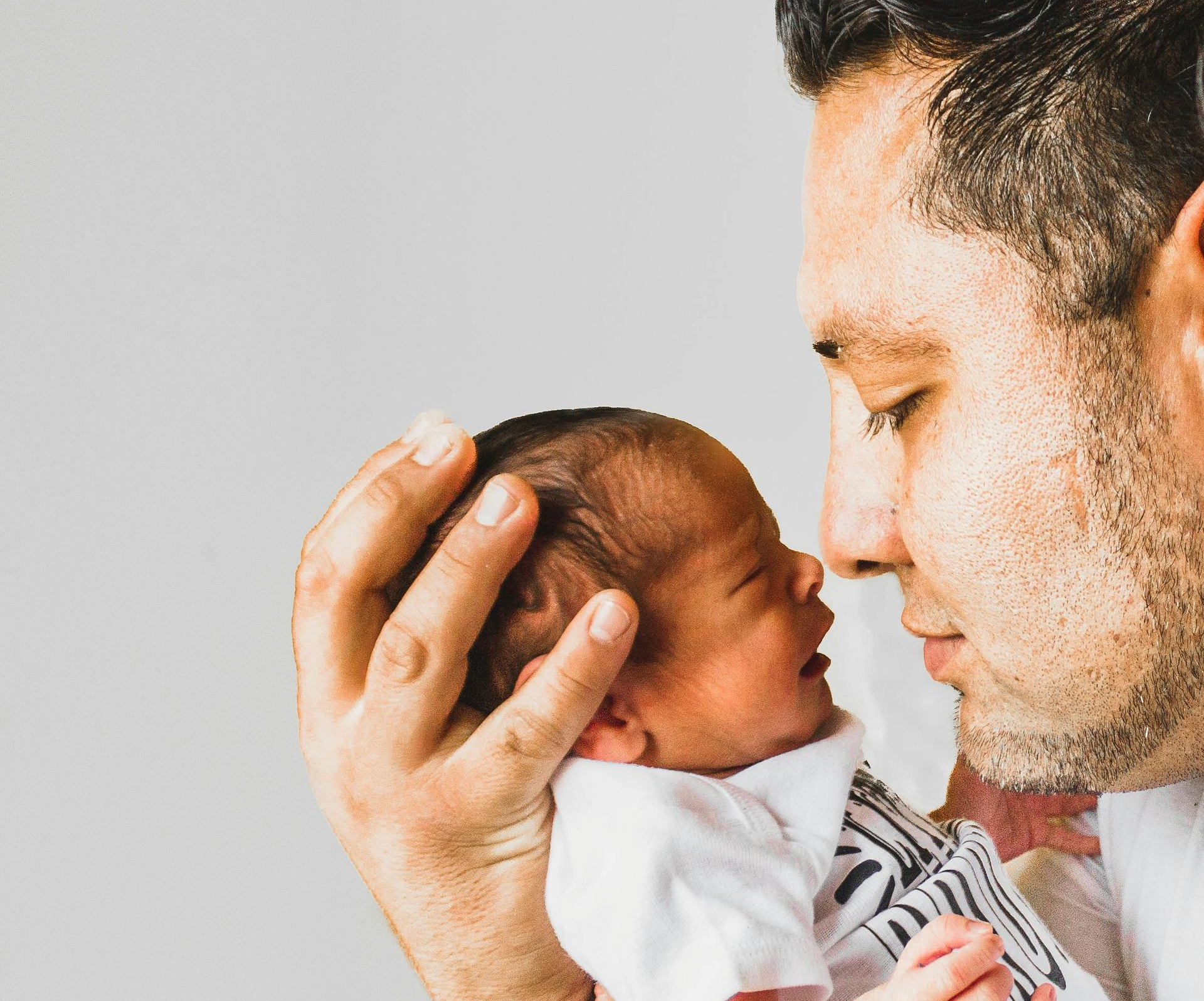 A parent holds an infant close to their face, smiling softly. A parent holds an infant close to their face, smiling softly.