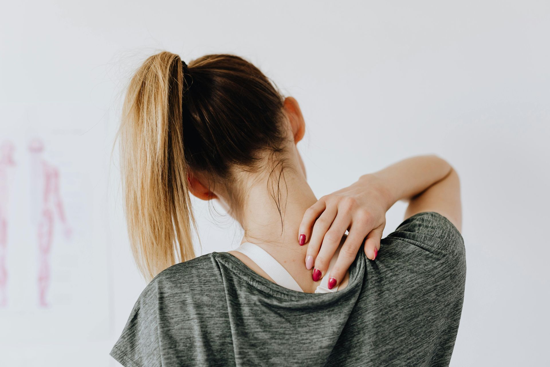 A person faces away from the camera and rubs the base of their neck to soothe pain.
