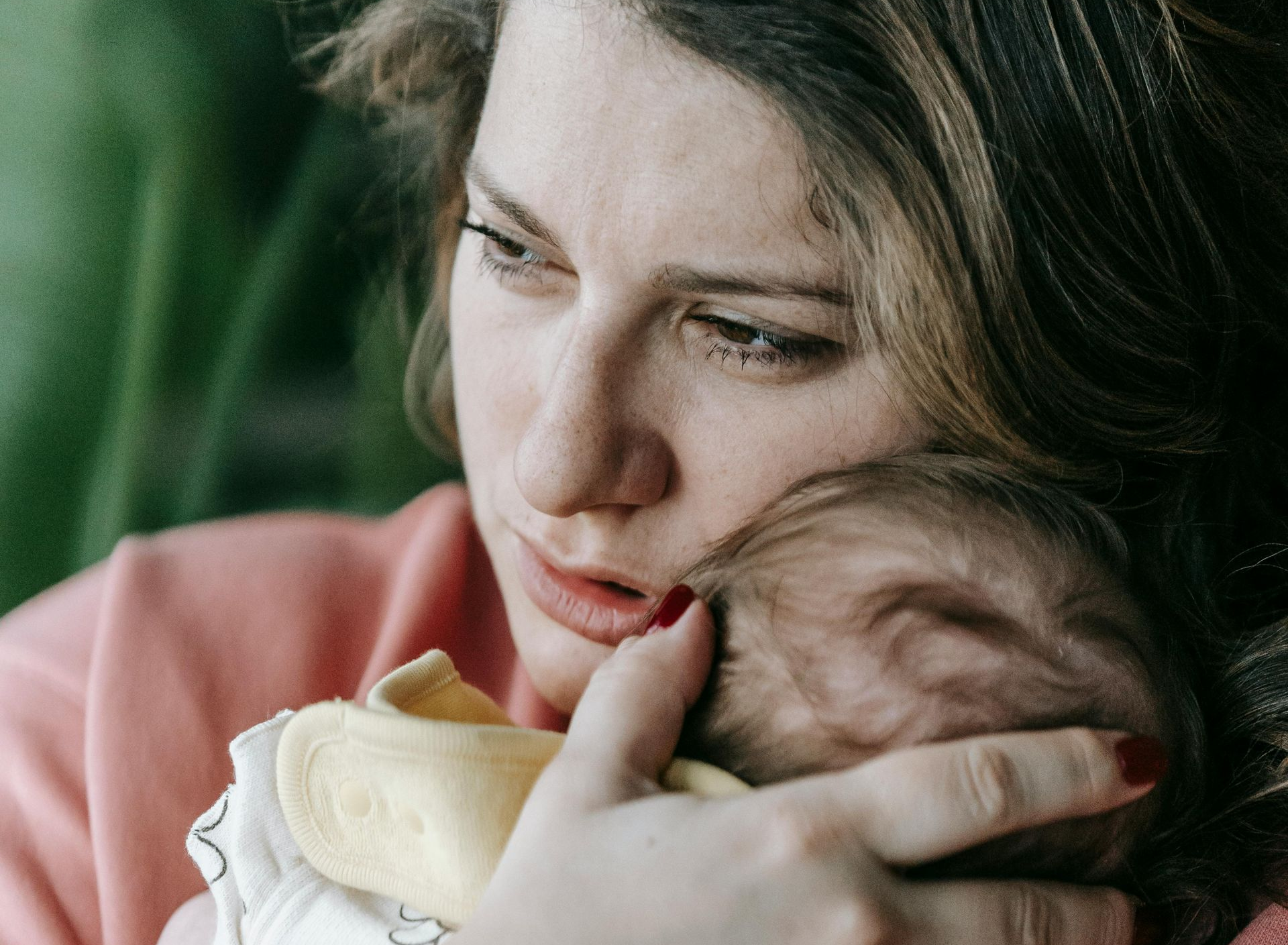 A parent holds an infant close to their face, expression solemn. A parent holds an infant close to their face, expression solemn.