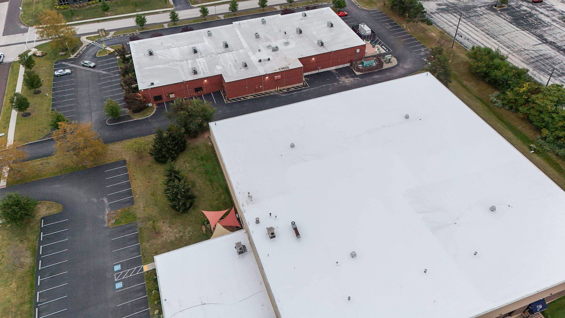 Aerial view of buildings, parking lots, and green space, likely a commercial or industrial area.