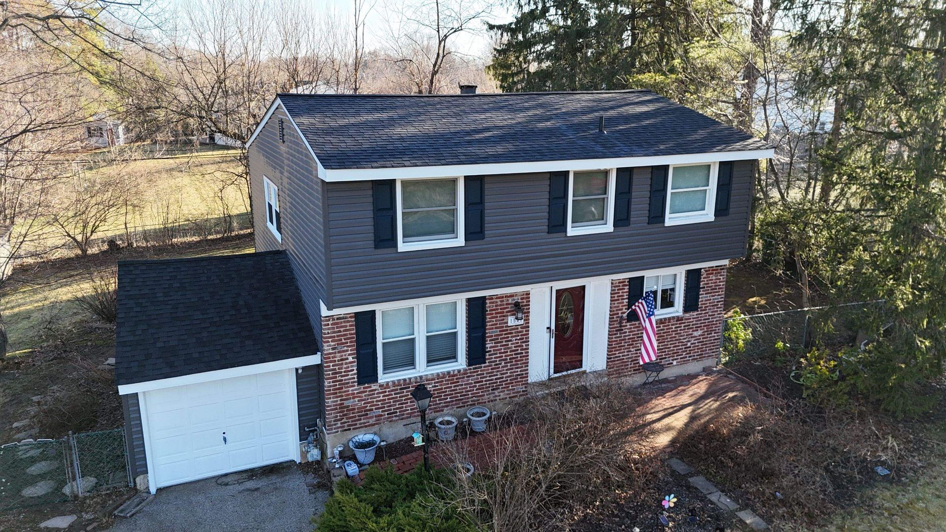 Two-story house with dark gray siding, brick lower level, a white attached garage, and an American flag near the front door.