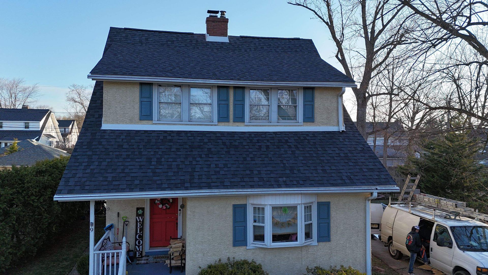 Two-story house with stucco exterior, blue shutters, a red door, and new dark shingles, with a van parked in the driveway.