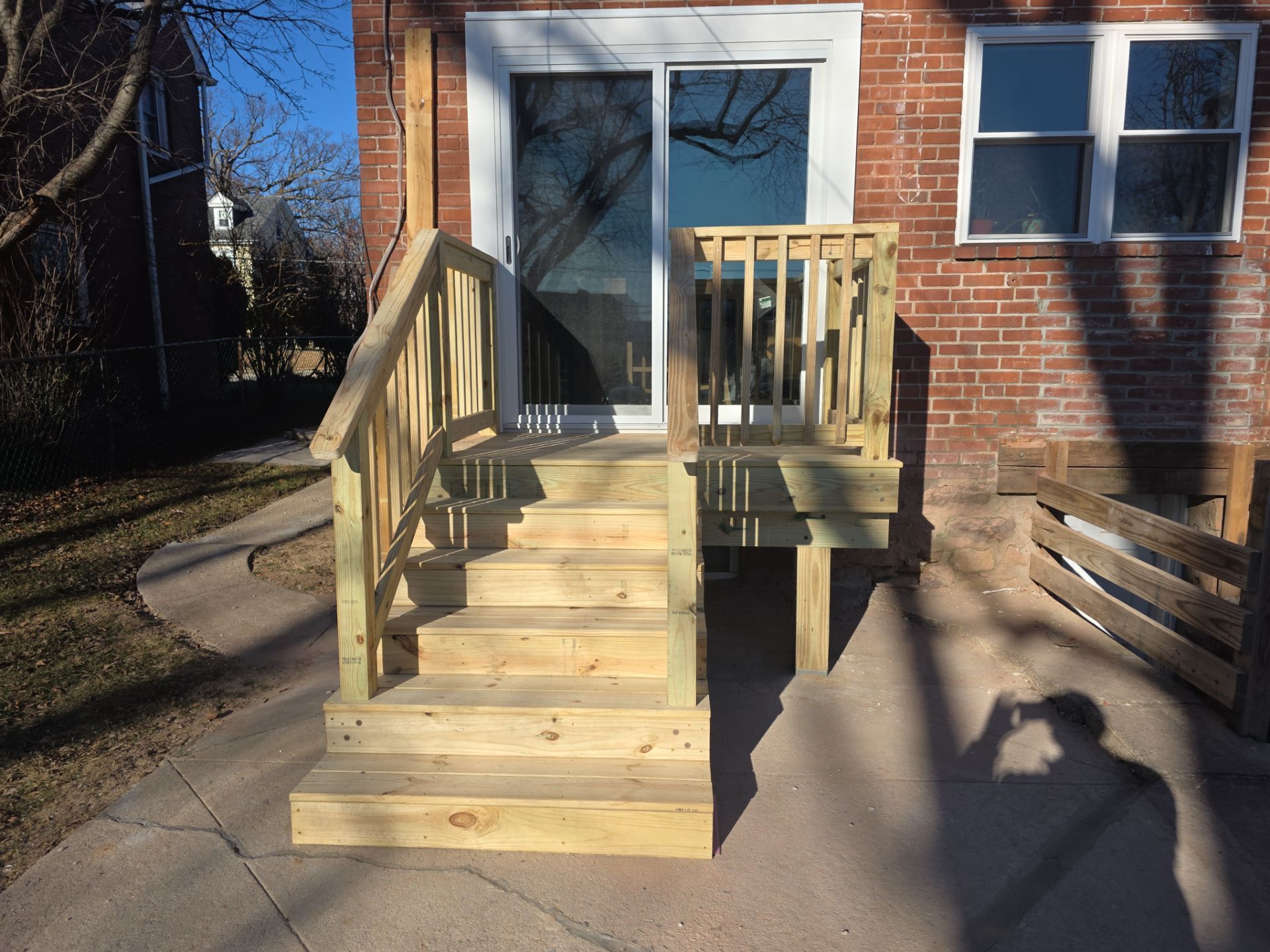 New wooden steps with railings leading up to a glass sliding door on a brick house.