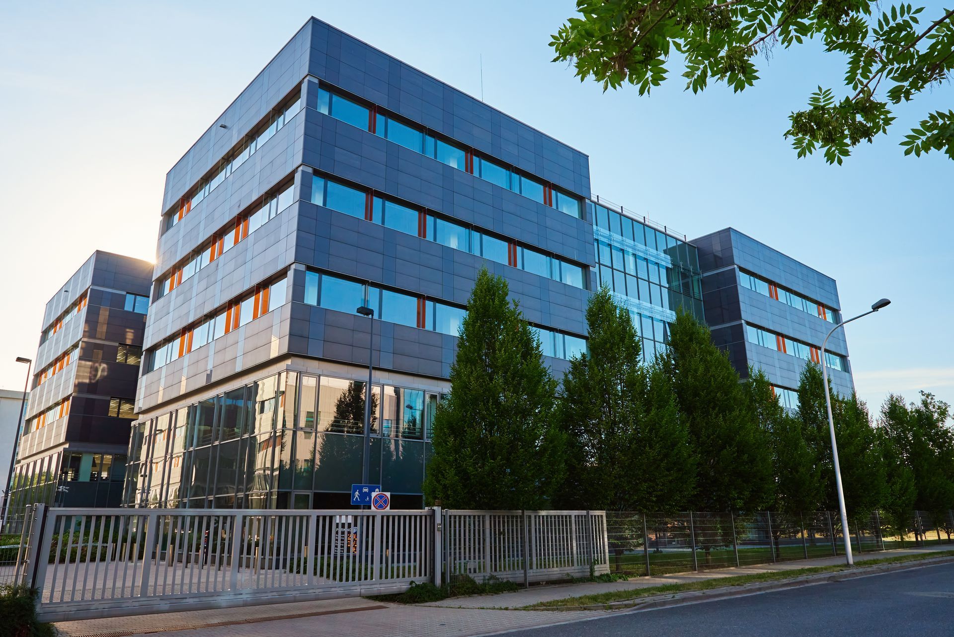 Modern office building with dark blue exterior and large windows, sunny day.