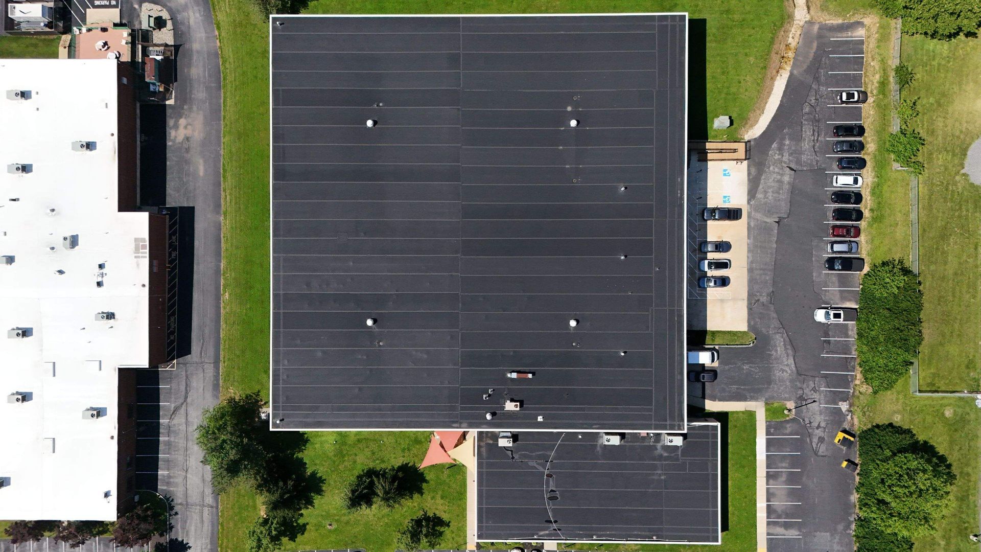 Flat, black tar roof with various vents and protrusions; distant buildings and trees.