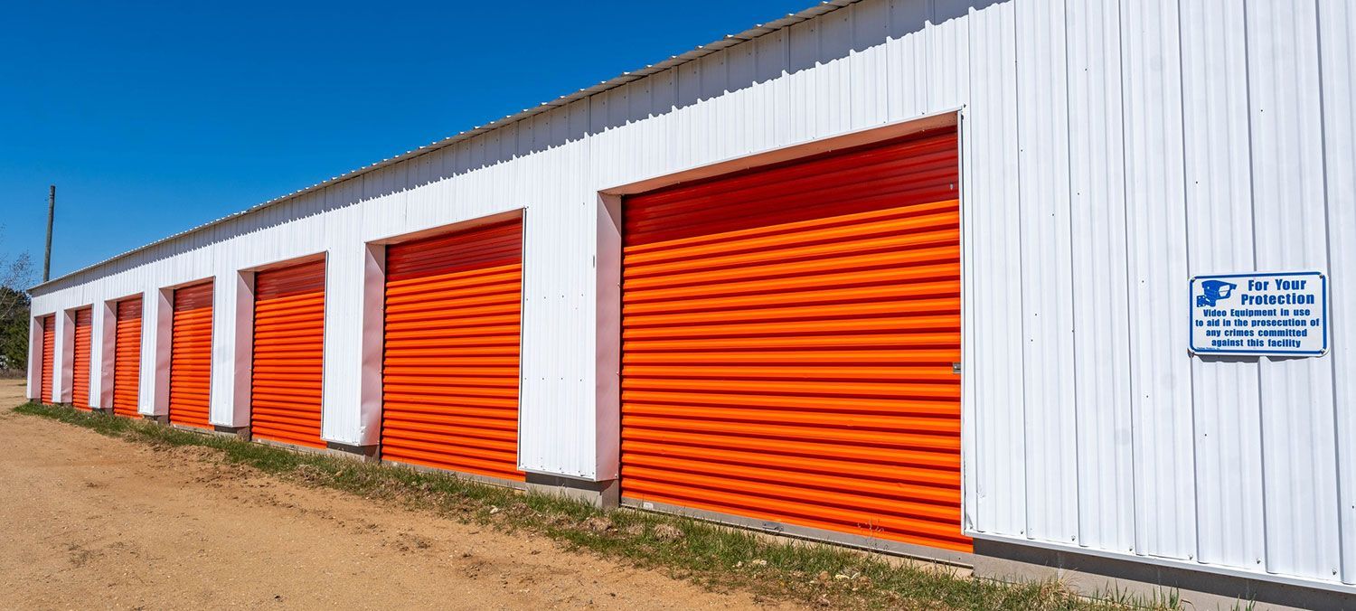 Storage units with orange doors and white walls under a blue sky.