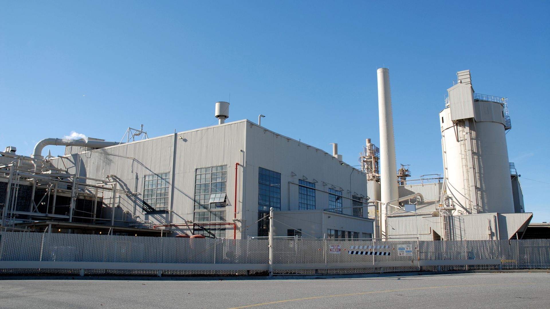 Industrial building complex with a tall chimney against a clear blue sky.