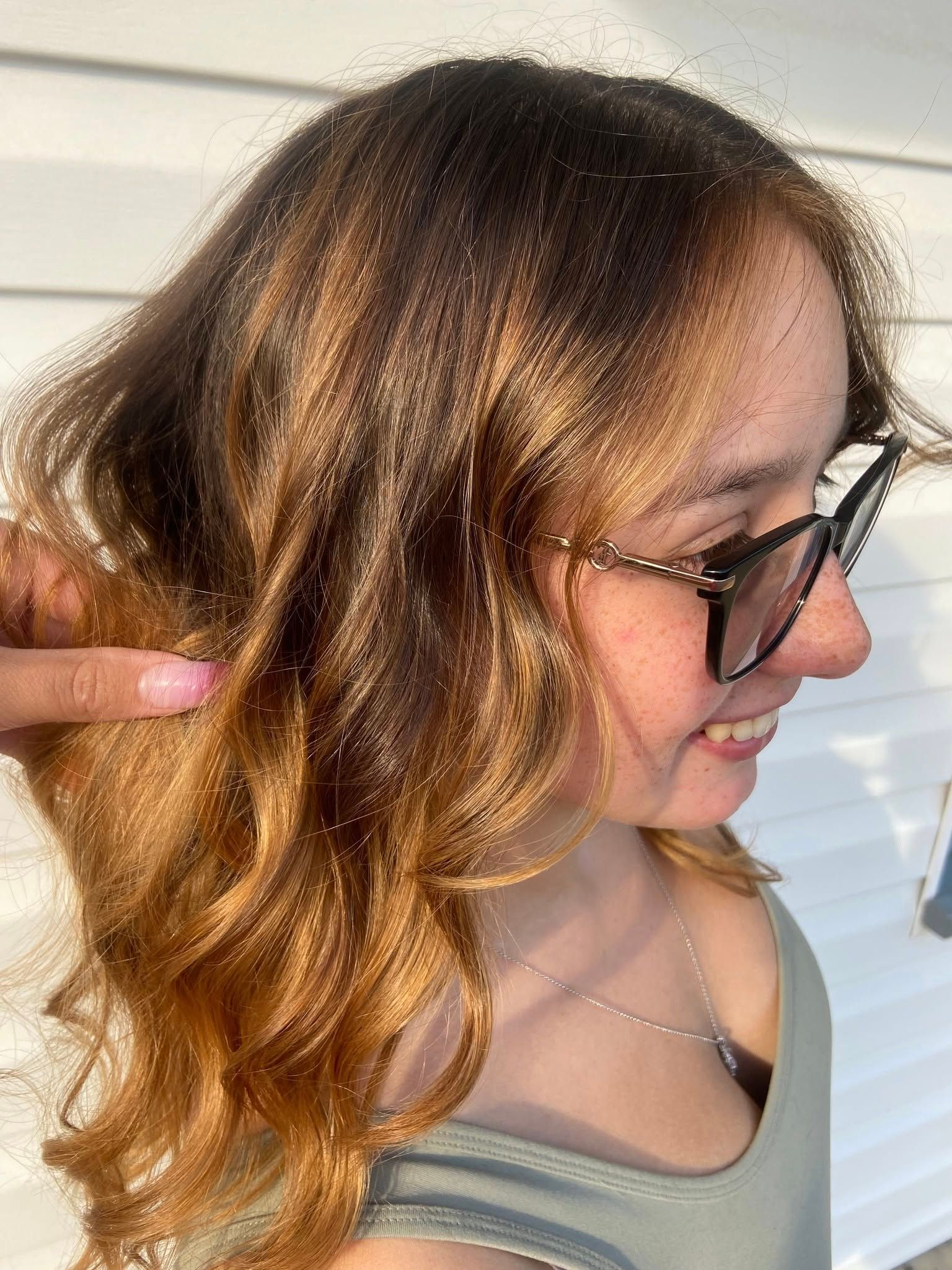 A woman wearing glasses and a tank top is pointing at her hair.