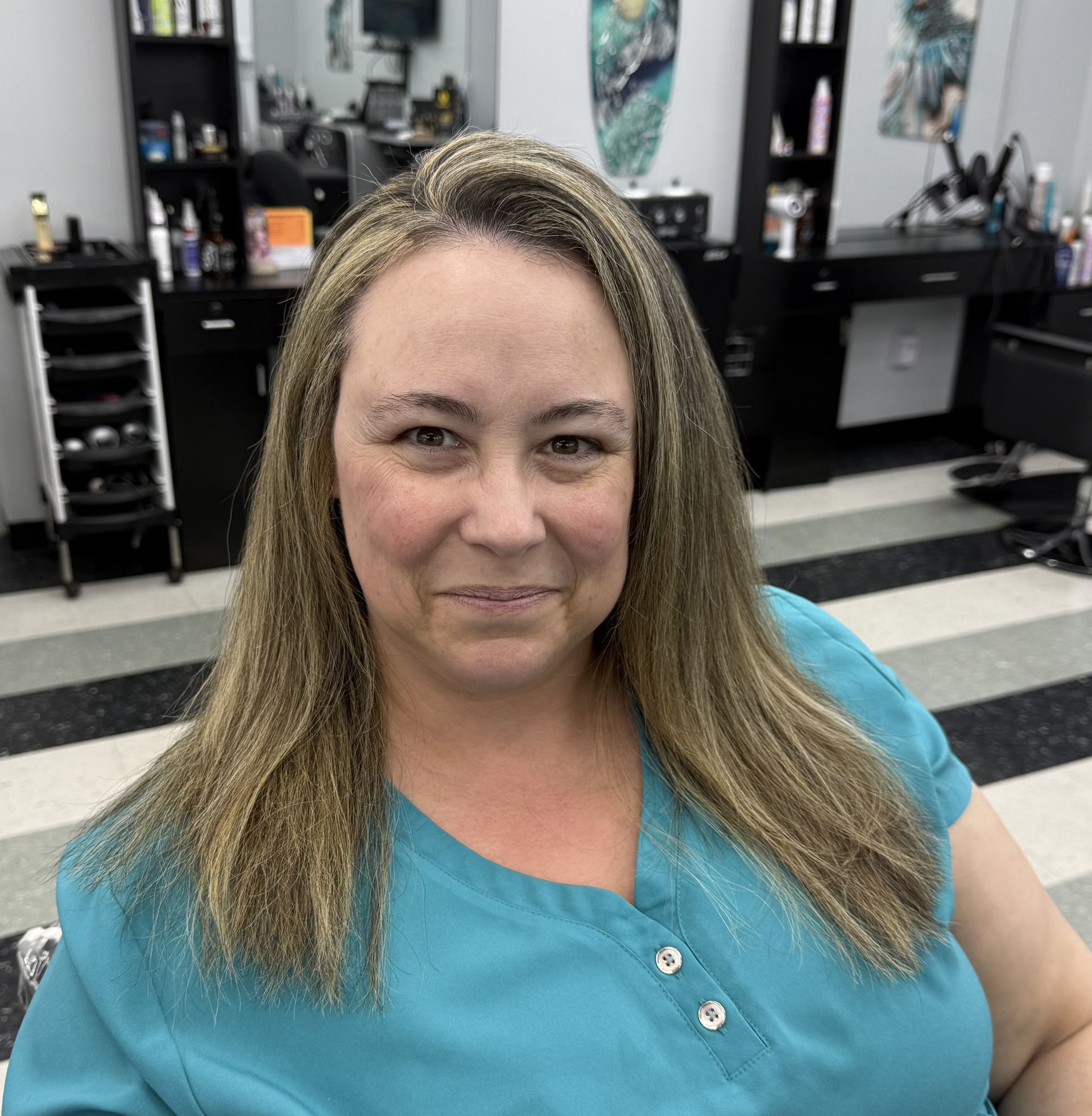 A woman in a blue shirt is smiling in a salon