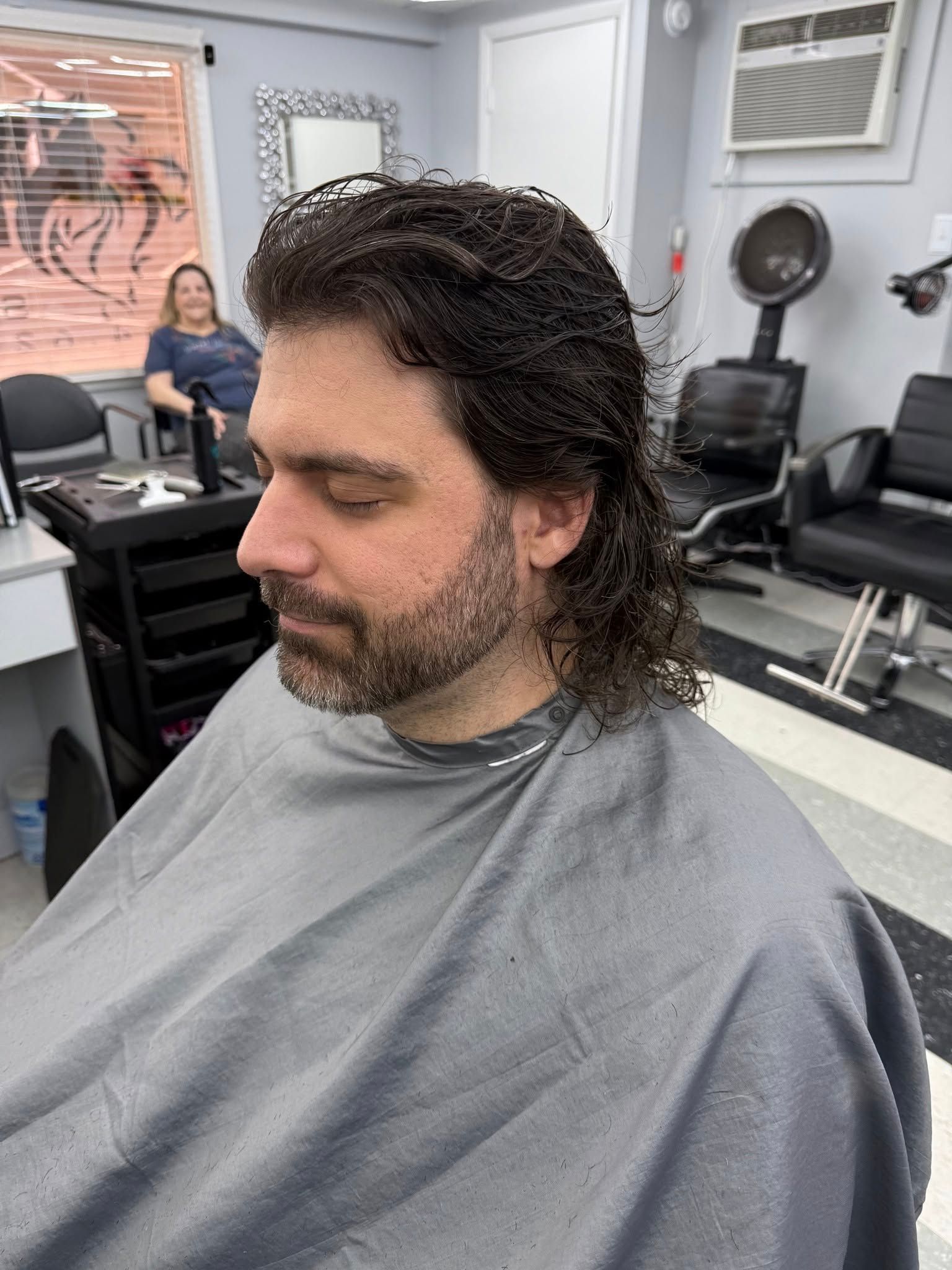 A man with a beard is getting his hair cut in a salon.