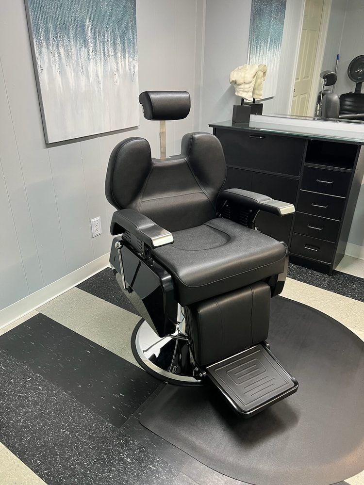 A black barber chair is sitting in a room next to a mirror.