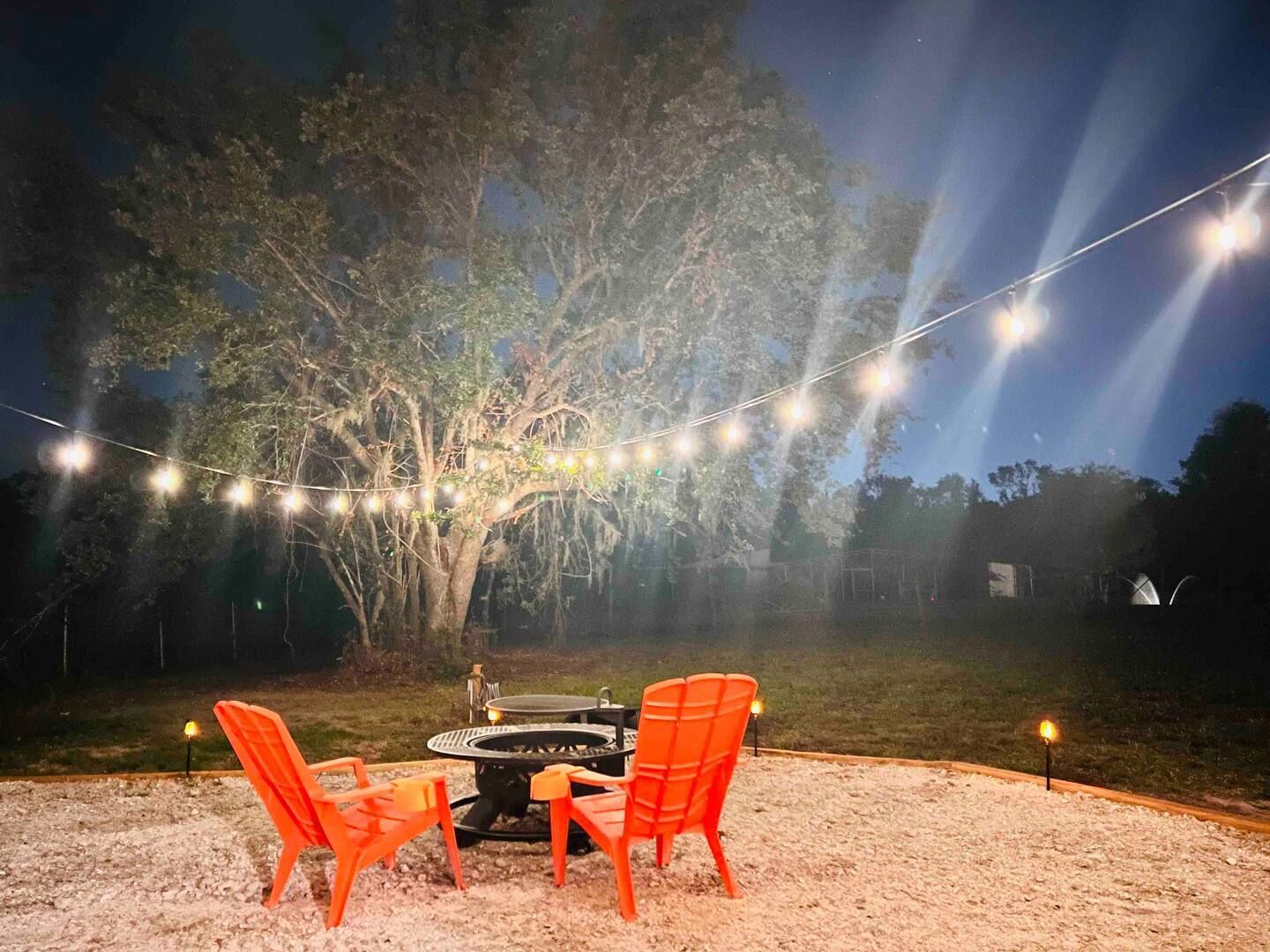 Two orange chairs are sitting in front of a fire pit at night.