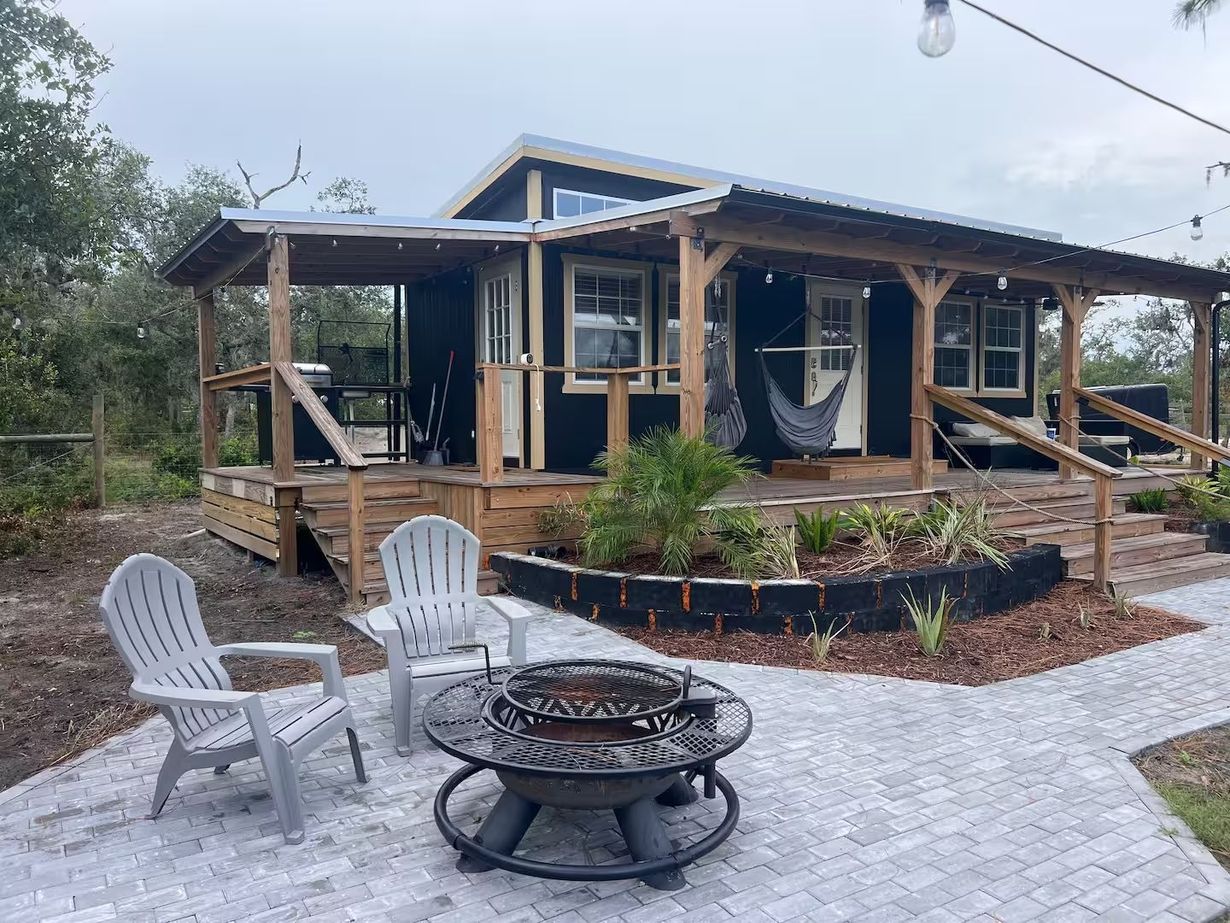 A house with a fire pit and chairs in front of it.