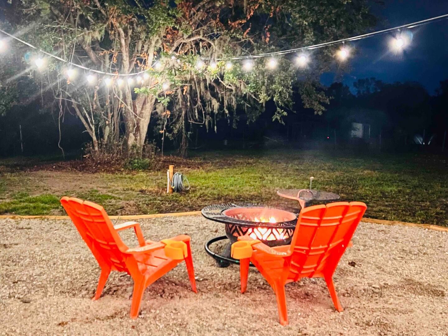 Two red chairs are sitting next to a fire pit at night.