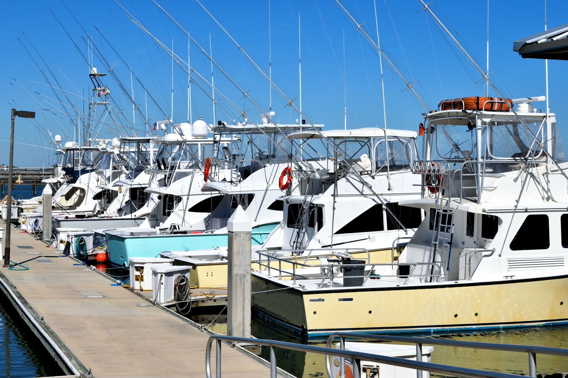 Boats docked at a marina on a sunny day. White and yellow boats with fishing rods lined up.