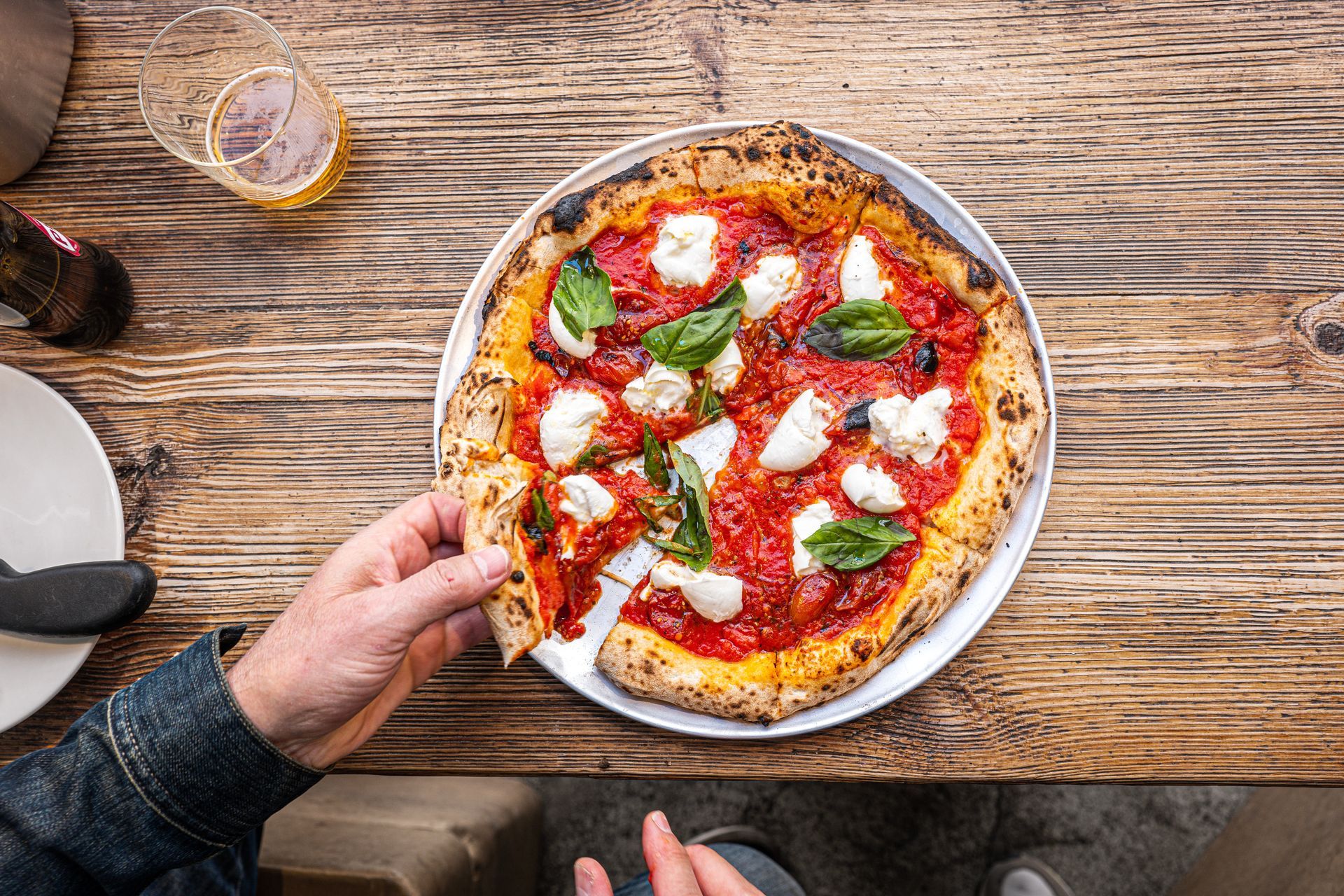 Person holding pizza slice from a Margherita pizza on a wooden table.