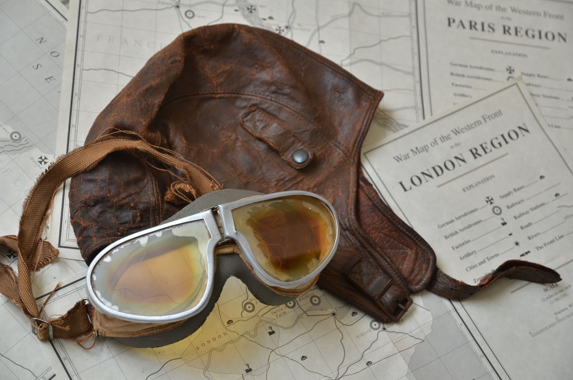 Vintage aviator goggles and leather helmet on a map of the London and Paris regions.