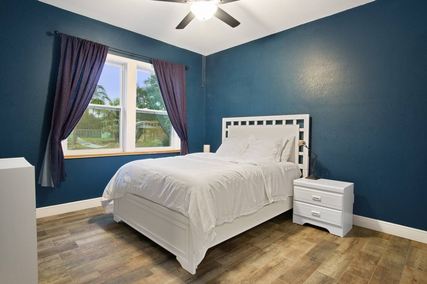 A bedroom with blue walls , a bed , a nightstand , and a ceiling fan.