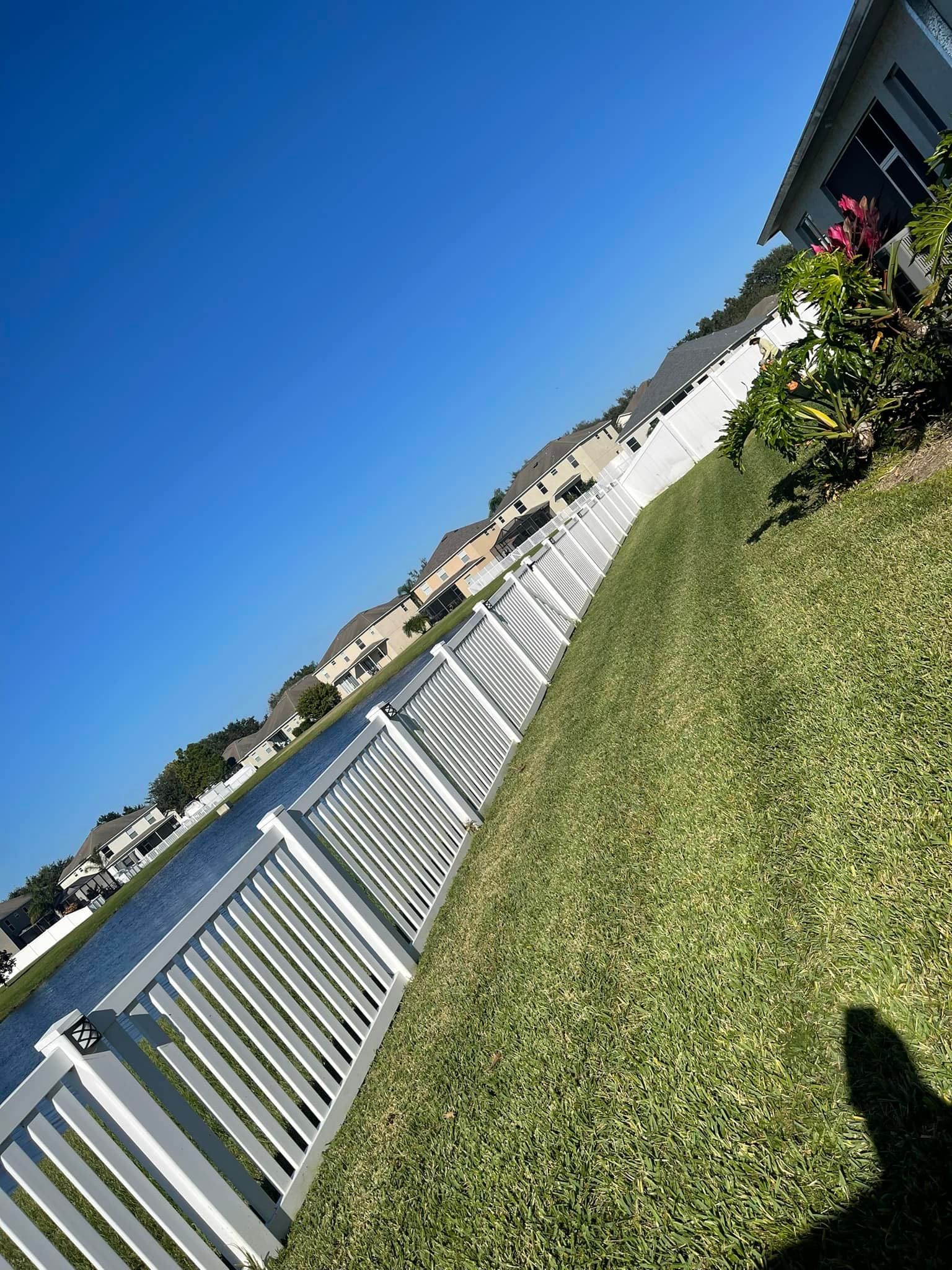 A white fence surrounds a lush green lawn next to a body of water.