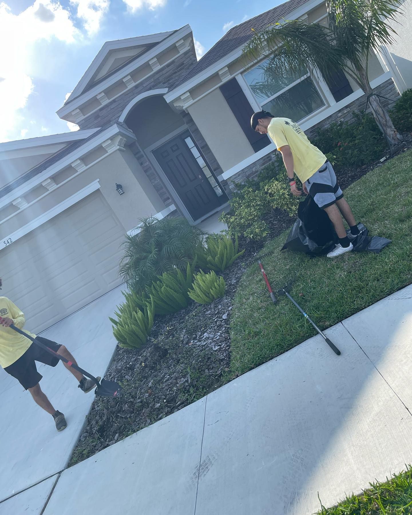 Two men are mowing the grass in front of a house.