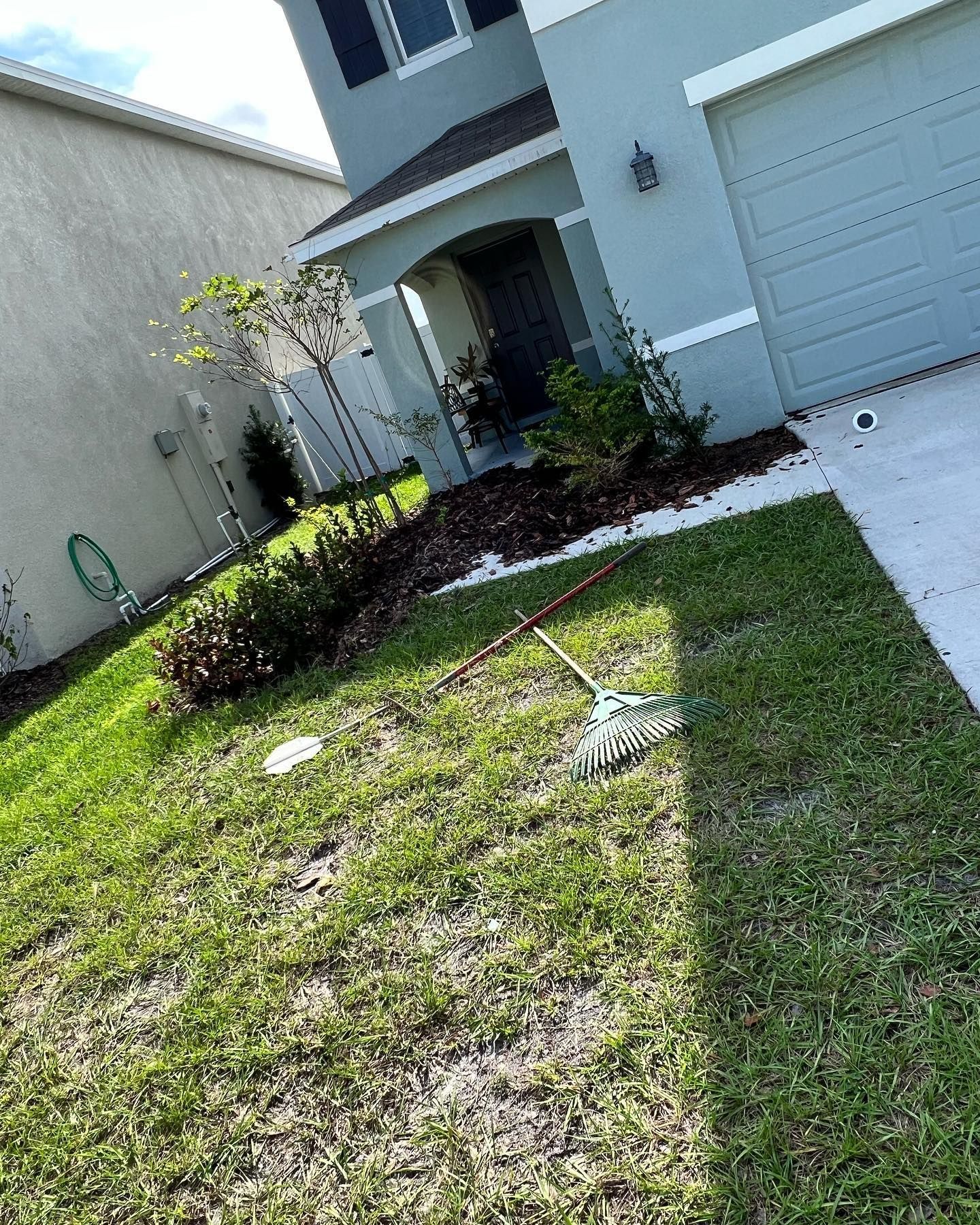 A rake is sitting in the grass in front of a house.