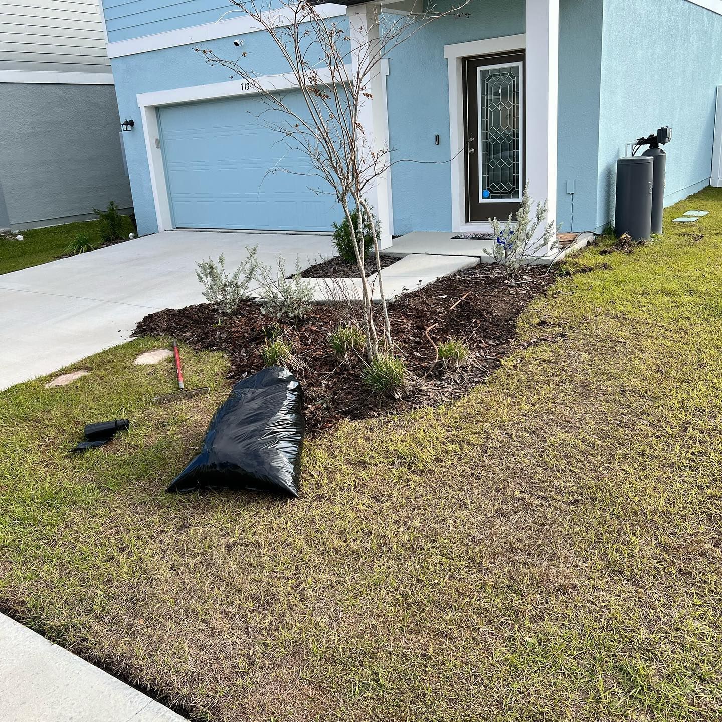 A bag of dirt is laying on the grass in front of a house.