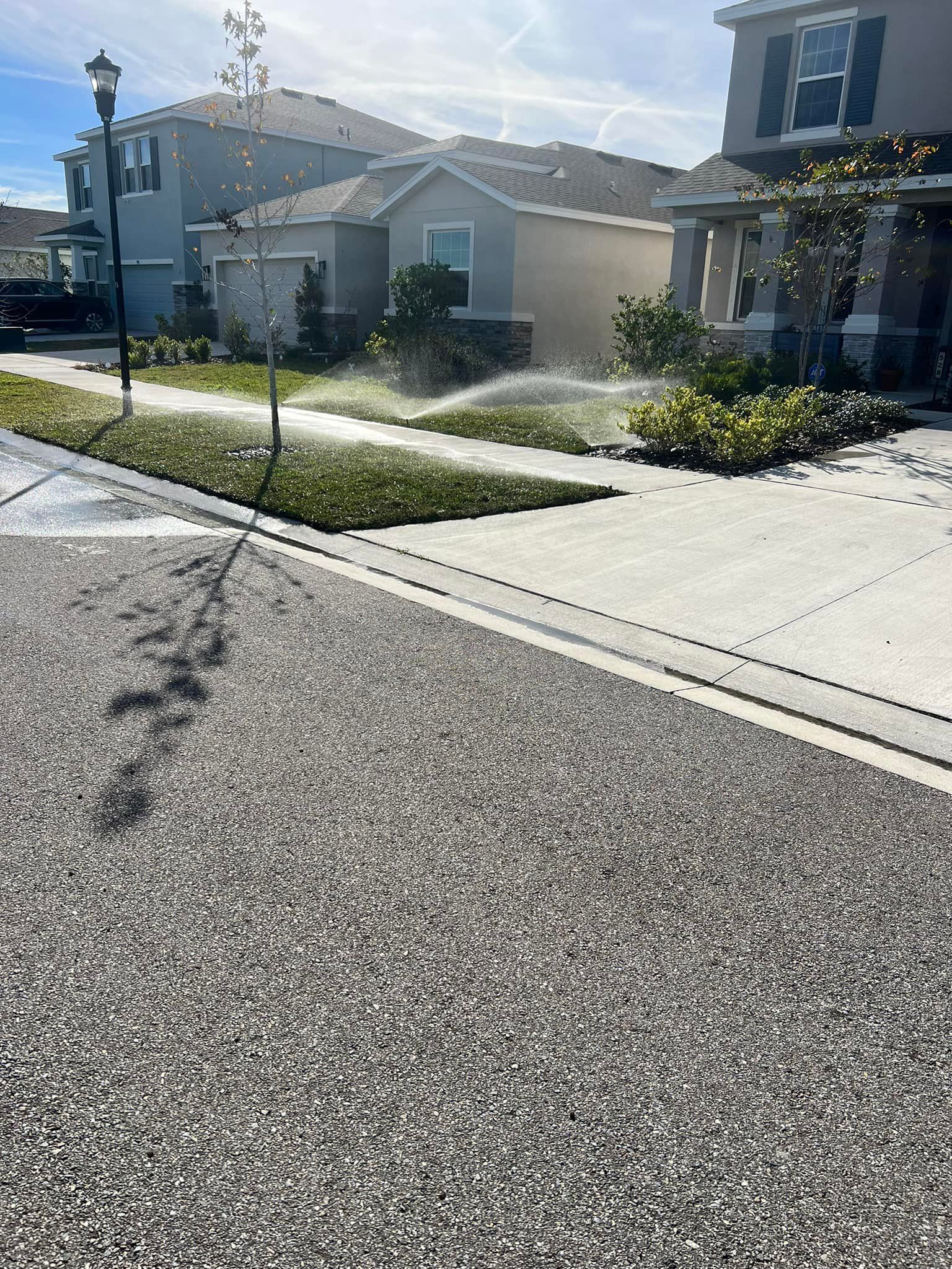 A sprinkler is spraying water on the grass in front of a house.