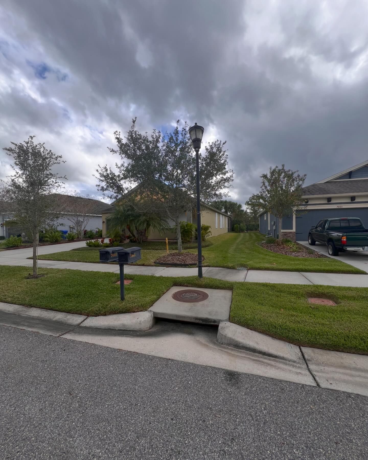 A green truck is parked in front of a house on a cloudy day
