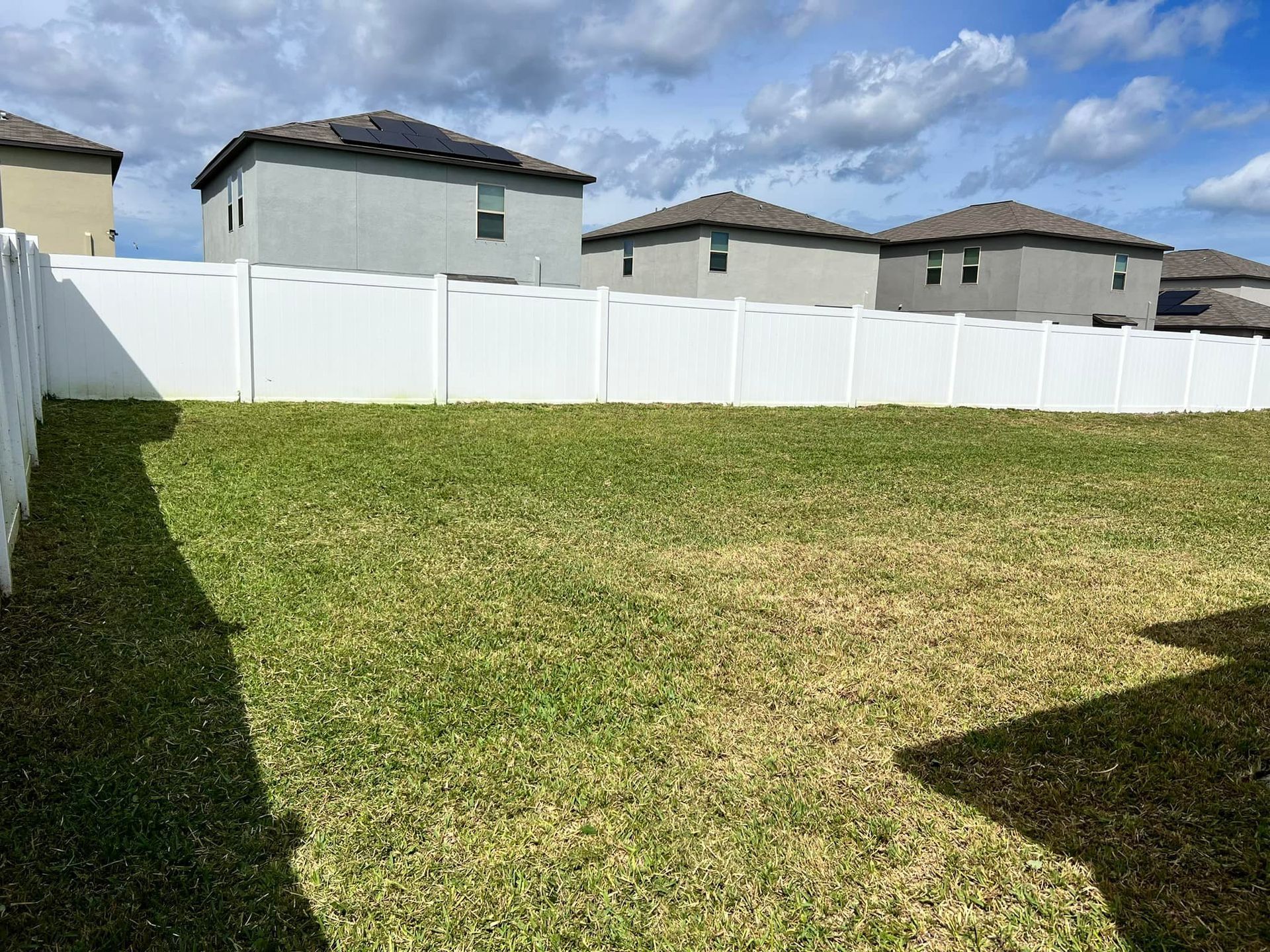 A backyard with a white fence and houses in the background.