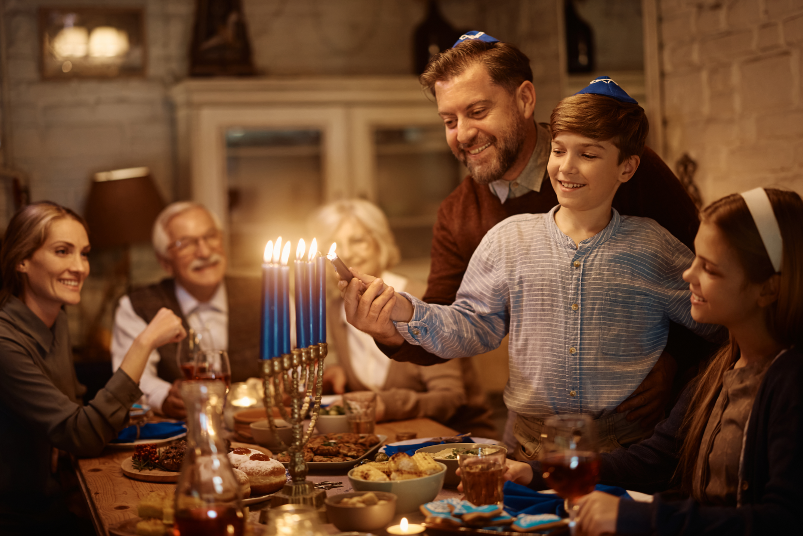 A family is sitting at a table lighting candles on a menorah.