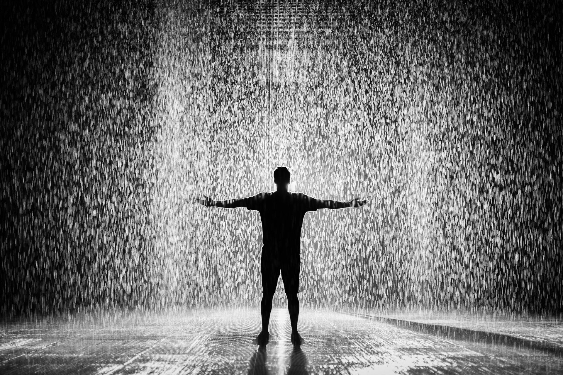 A man is standing in the rain with his arms outstretched.