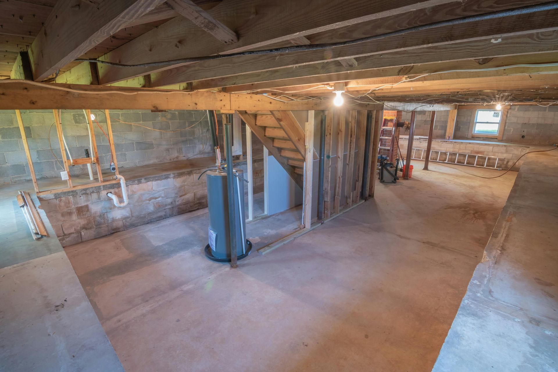 An empty basement with a staircase and a water heater, ready for drywall to make usable space.