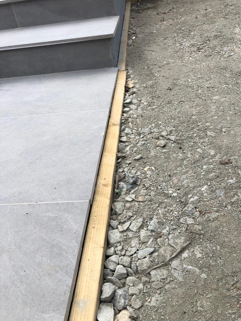 A wooden border between a tiled walkway and gravel.