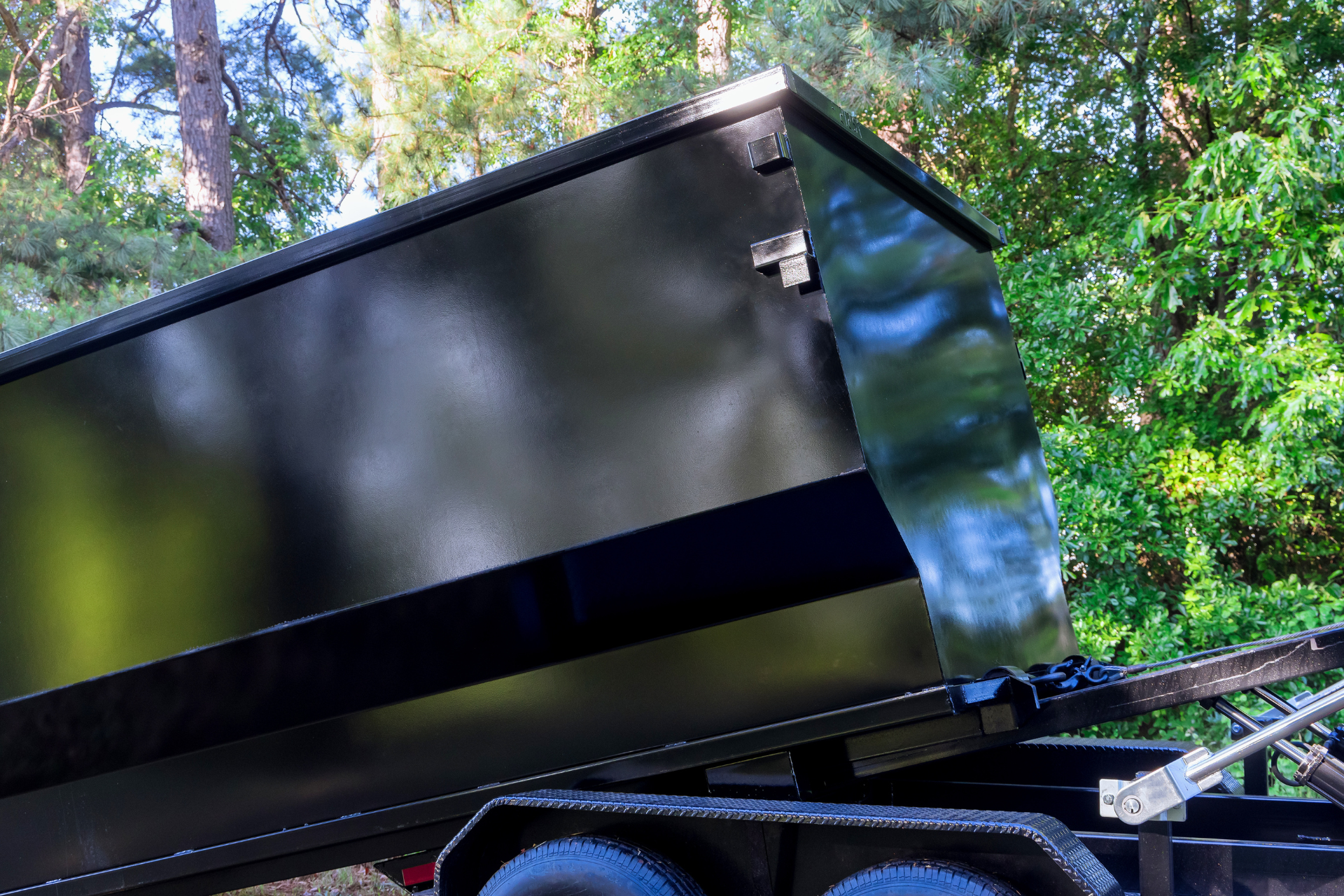 A large black dumpster is sitting in the grass in front of a house.