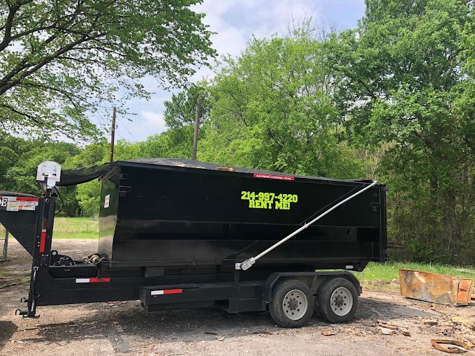 An Iron Man Roll Offs dumpster trailer is parked in a dirt lot next to trees.