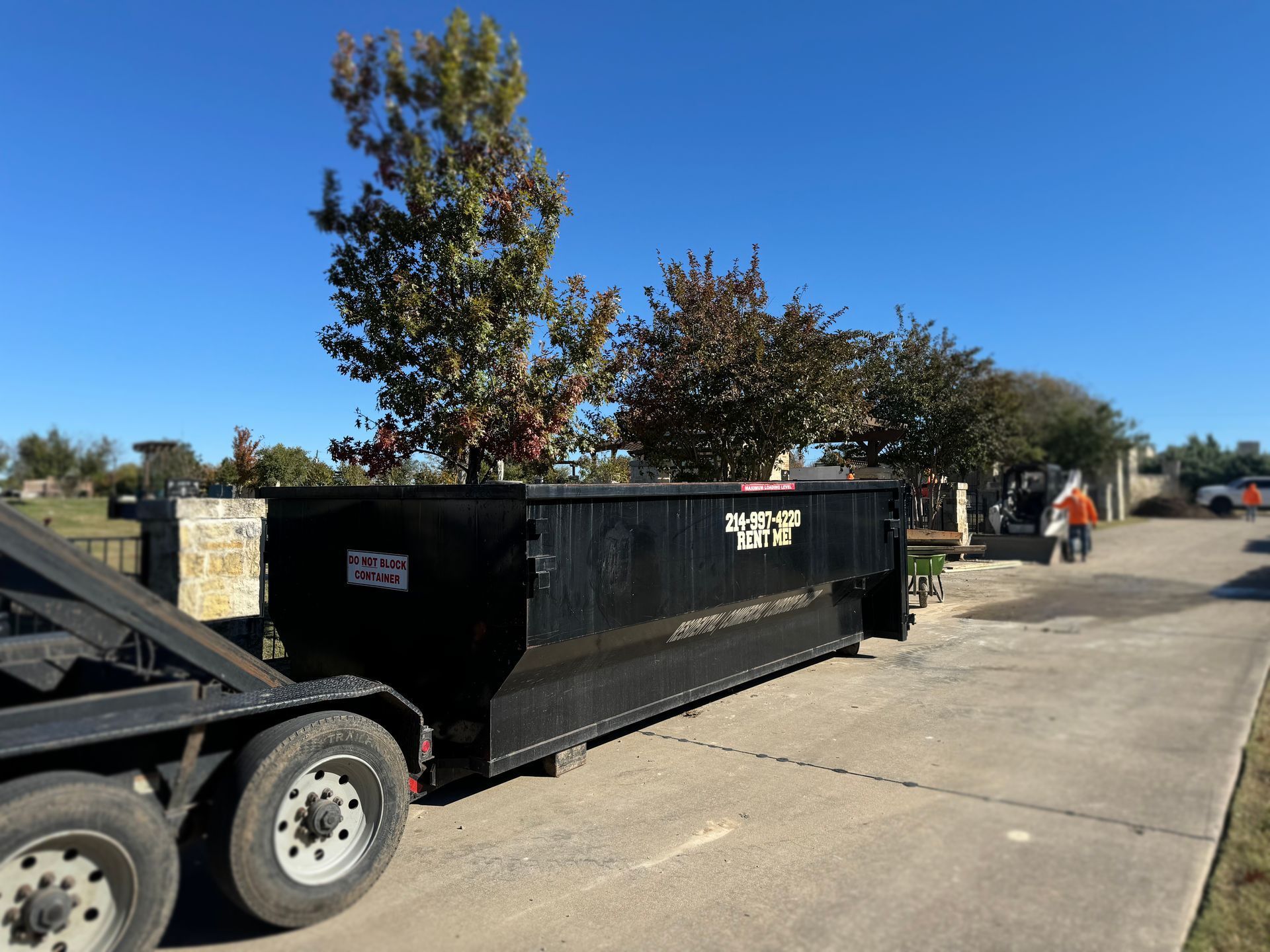 A dumpster is sitting on the side of the road next to a trailer.