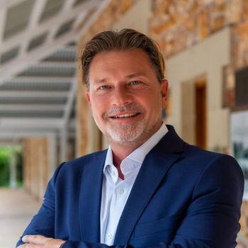 A man in a blue suit and white shirt is standing with his arms crossed.