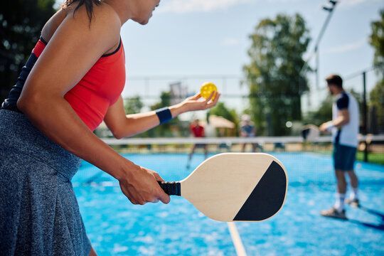 A woman is holding a paddle and a tennis ball on a tennis court.