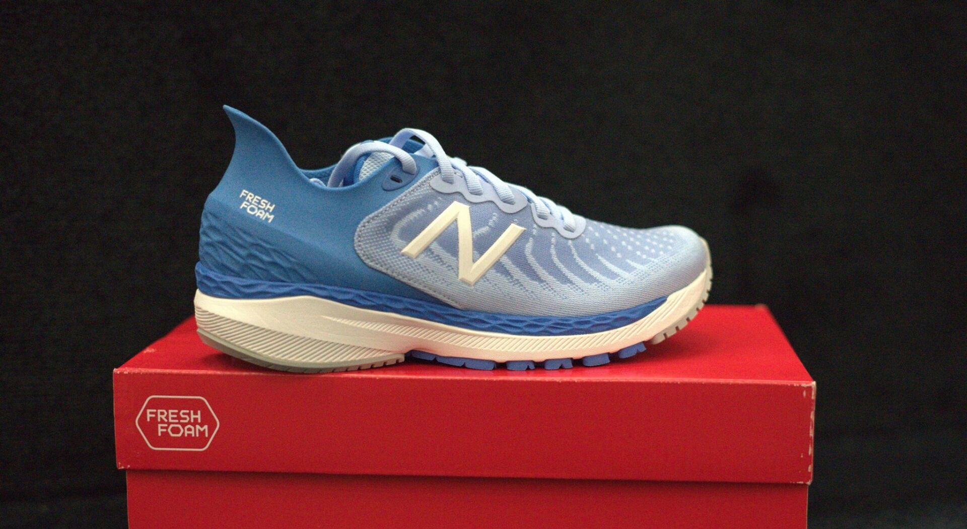 A pair of blue and white new balance shoes are sitting on top of a red box.