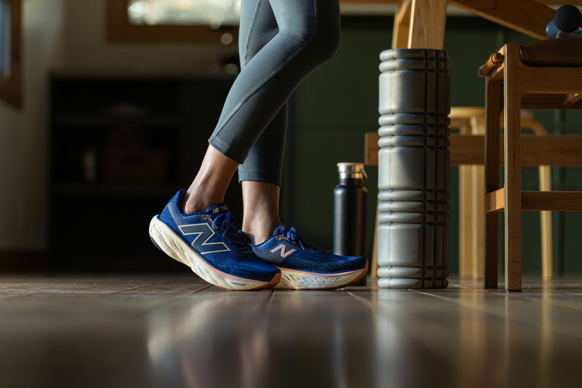A person wearing blue shoes is standing next to a foam roller on the floor.