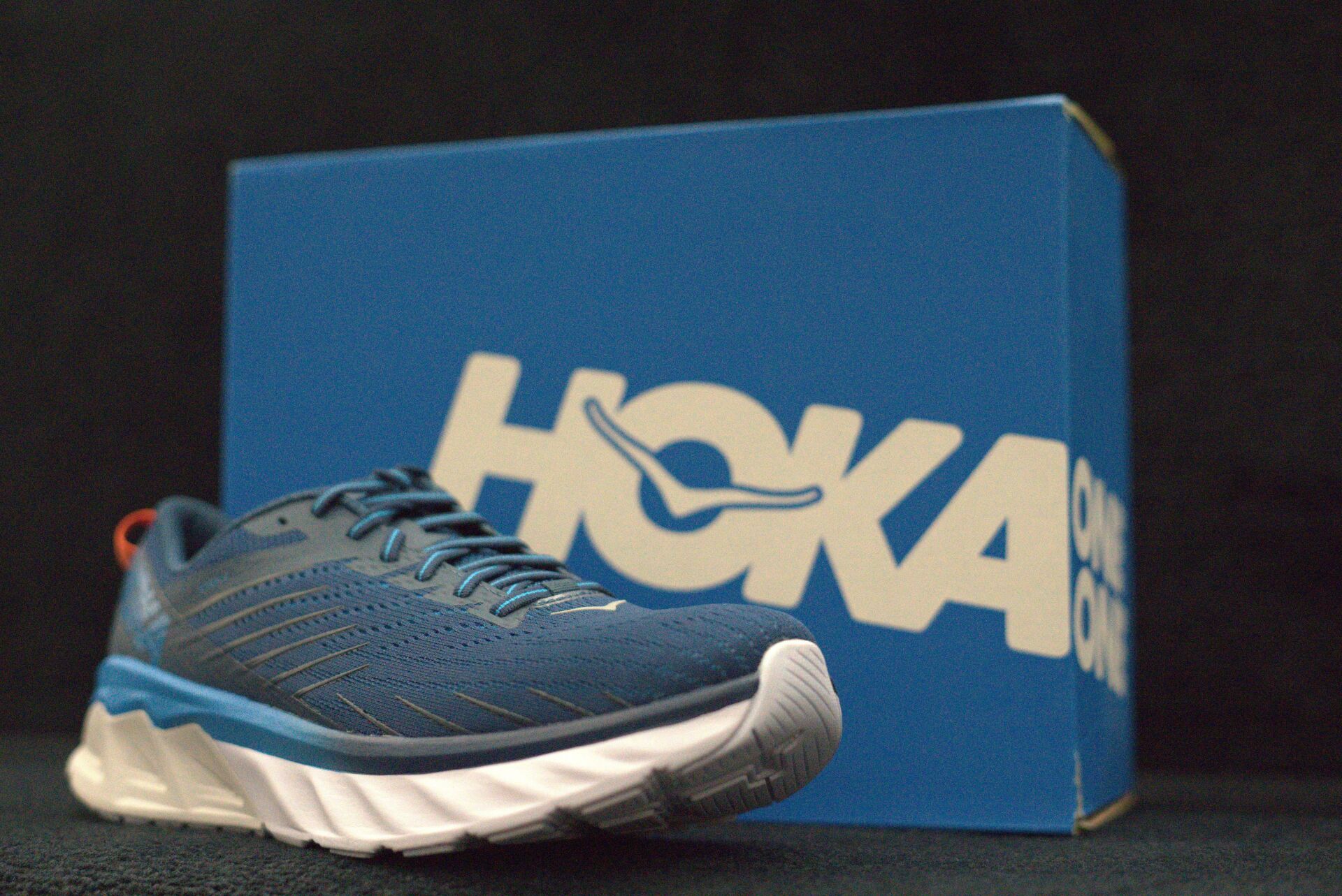 A pair of hoka shoes sitting in front of a blue box