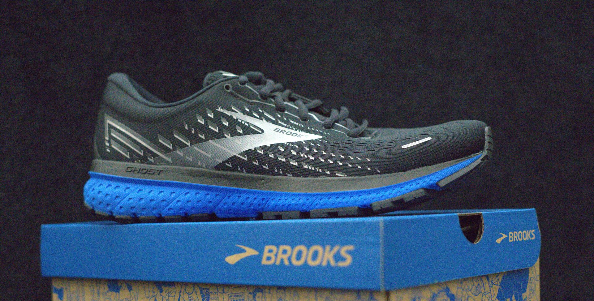 A pair of black and blue brooks running shoes sitting on top of a blue box.