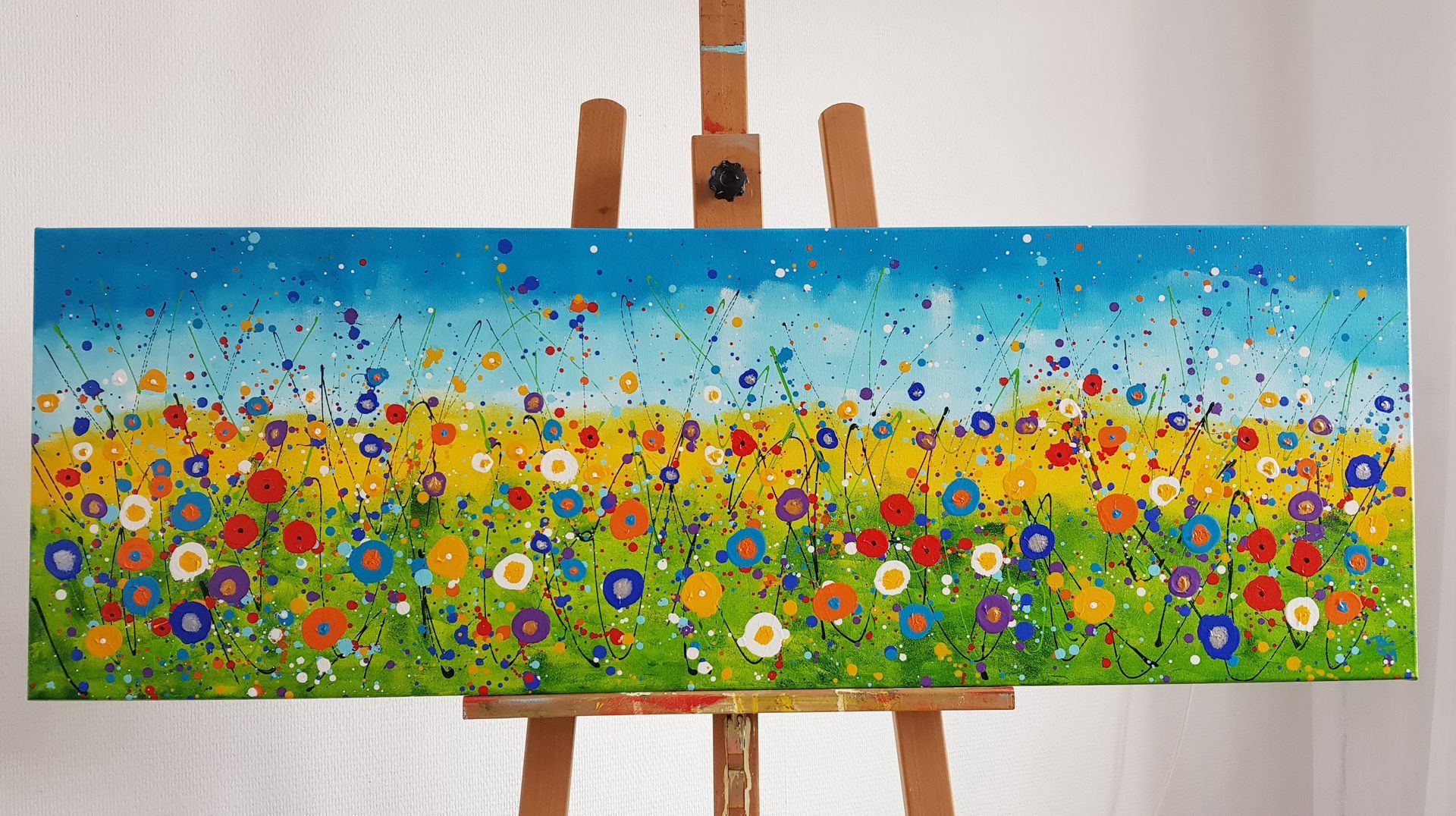 Kleurrijk schilderij van een veld met wilde bloemen op een canvas, onder een blauwgespikkelde lucht, op een houten ezel. Creatieve workshop.